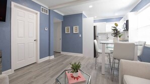 Una sala de estar moderna con comedor, que incluye una mesa de centro de vidrio, un sofá y una cocina al fondo.