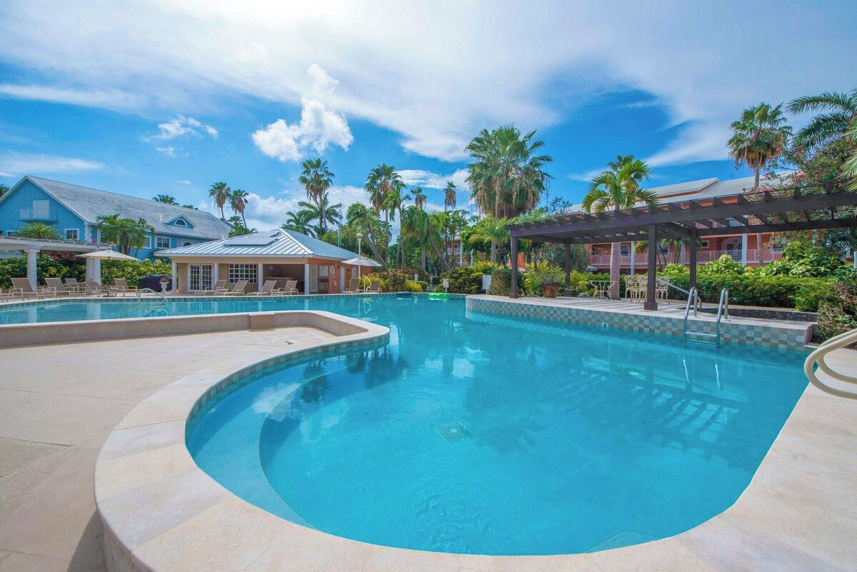 A swimming pool with a curved edge, surrounded by lounge chairs and a covered area with a pergola.