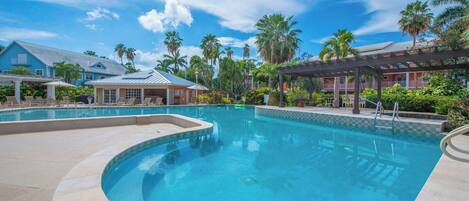 A swimming pool with a curved edge, surrounded by lounge chairs and a covered area with a pergola.