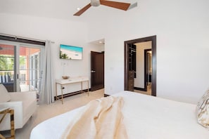 Quarto de hotel com cama, escrivaninha, cadeira, ventoinha no teto e vista para o exterior.