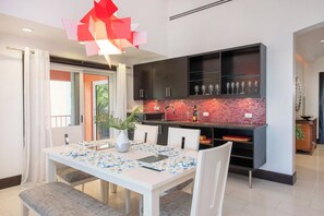A modern kitchen with dark cabinets, a red tiled backsplash, and a dining area with a white table and chairs.