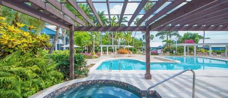 A pool area with a pergola overhead, surrounded by lush greenery and palm trees.