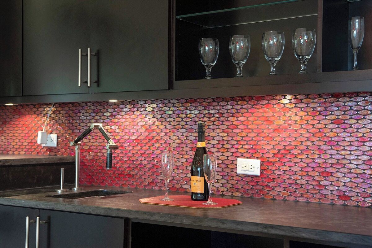 A kitchen with a tiled backsplash, a wine bottle, and two glasses on a mat.