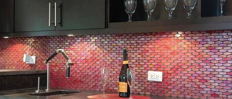 A kitchen with a tiled backsplash, a wine bottle, and two glasses on a mat.