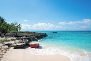 Una playa con agua turquesa cristalina, un bote rojo en la orilla y afloramientos rocosos.