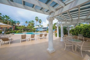 A poolside area with lounge chairs and a covered seating area. - Canal Front 3BR Condo on 7 Mile Beach - Britannia 634 (Brittania)