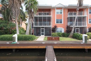 A multi-story building with balconies, a wooden dock, and a water body in front. - Canal Front 3BR Condo on 7 Mile Beach - Britannia 634 (Brittania)
