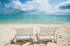 Two white beach chairs facing a turquoise sea under a partly cloudy sky.
