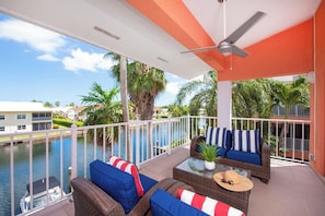 A balcony with wicker furniture, a view of a water body, and a white railing.