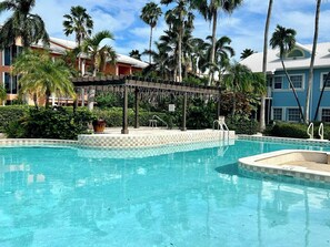 A swimming pool with a checkered edge, surrounded by palm trees and a covered seating area.
