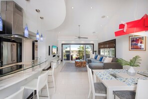 A modern kitchen with a glass-top dining table, white chairs, and a built-in oven.