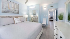 Une chambre à coucher comprenant un lit, un ventilateur de plafond, une table de chevet, une chaise, une commode et un miroir.
