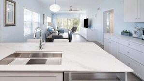 Une cuisine moderne dotée d’un grand îlot central, de meubles blancs et d’un ventilateur de plafond.