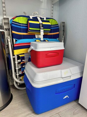 Varastotila, jossa on sininen kylmälaukku, punainen Rubbermaid-kylmälaukku ja värikäs raidallinen kassi.
