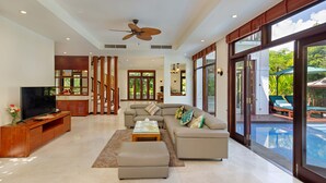 A spacious living room with a large sectional sofa, a flat-screen TV, and a ceiling fan. - Luxury Danang Beach Pool Villa (Da Nang)