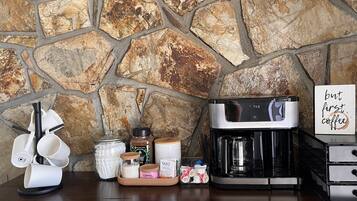 A kitchen counter with a coffee maker, mugs, and containers.