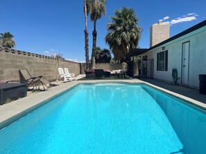 A rectangular swimming pool with clear blue water, surrounded by a concrete deck. There are lounge chairs and a small table on the deck. - HEATED Pool, Spacious home 7 MIN to airport* (Las Vegas)