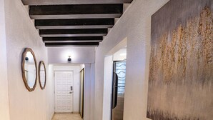 Een gang met een betegelde vloer, een witte deur en een schilderij aan de rechtermuur.