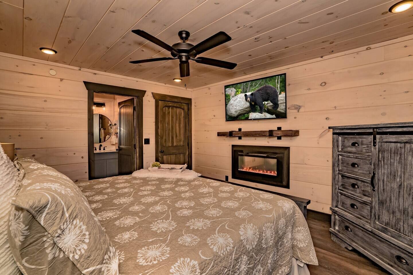 A bedroom with a bed, a fireplace, a television, and wooden walls.