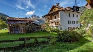 Ein traditionelles Chalet mit Holzbalkon, umgeben von üppigem Grün und Bergen im Hintergrund.