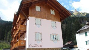 Ein mehrstöckiges Gebäude mit einem Holzbalkon und einem Steinunterbau, umgeben von Bergen.