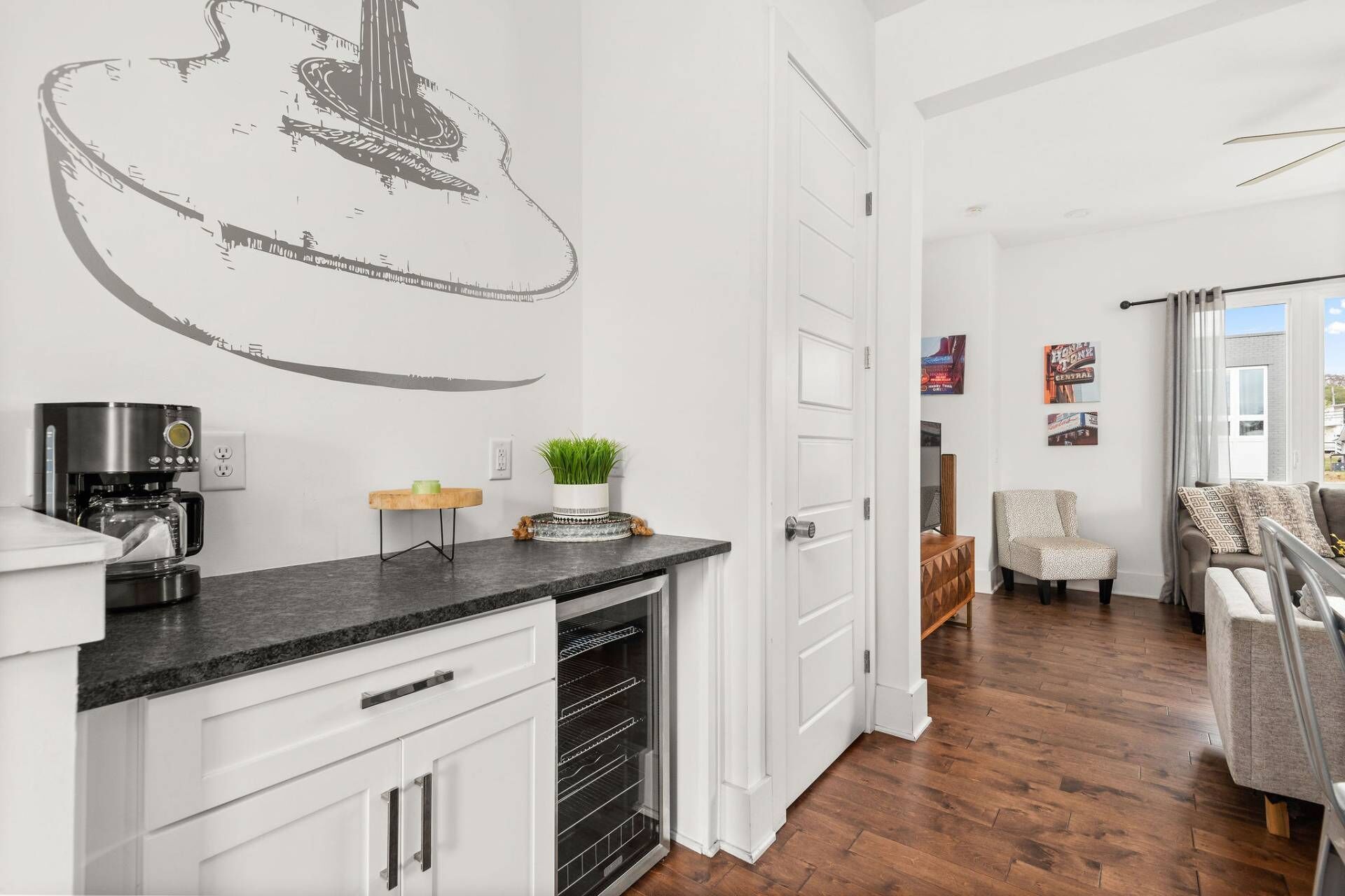 A modern kitchen with white cabinetry, a coffee machine, and a decorative guitar wall art.