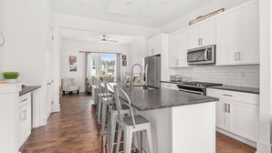 A modern kitchen with white cabinetry, a central island with bar stools, a stainless steel refrigerator, and a microwave. - V831 ~ East Nashville Charm ~ 11 Beds ~ 4 miles to Downtown and Broadway ~ WiFi ~ Garage Parking (Nashville)