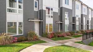 A modern apartment building with grey and white exterior walls, numbered units, and a well-maintained garden with flowers and shrubs. - V831 ~ East Nashville Charm ~ 11 Beds ~ 4 miles to Downtown and Broadway ~ WiFi ~ Garage Parking (Nashville)
