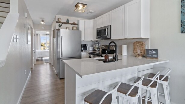 A modern kitchen with white cabinetry, a central island with bar stools, stainless steel appliances, and a decorative sign.