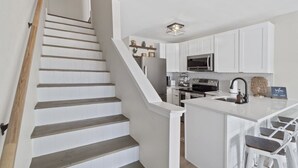 A modern kitchen with white cabinetry, a central island, and a staircase with wooden steps.