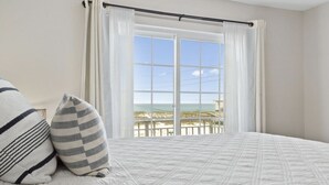 A bedroom with a large window, a bed with a quilt, and two pillows.