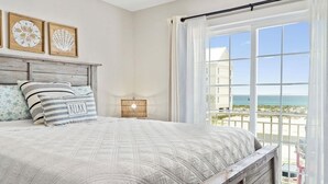 A bedroom with a large bed, a wooden headboard, and a view of the beach through a window.