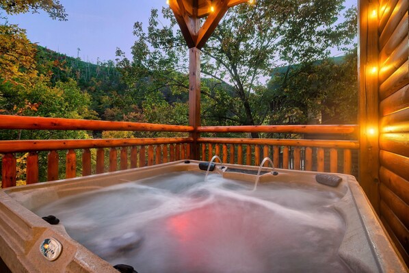 A hot tub with a wooden deck and a view of a forested hillside.