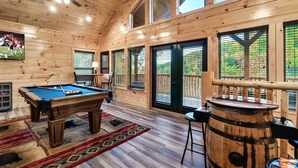 Un intérieur en bois avec une table de billard, un coin bar et de grandes fenêtres.