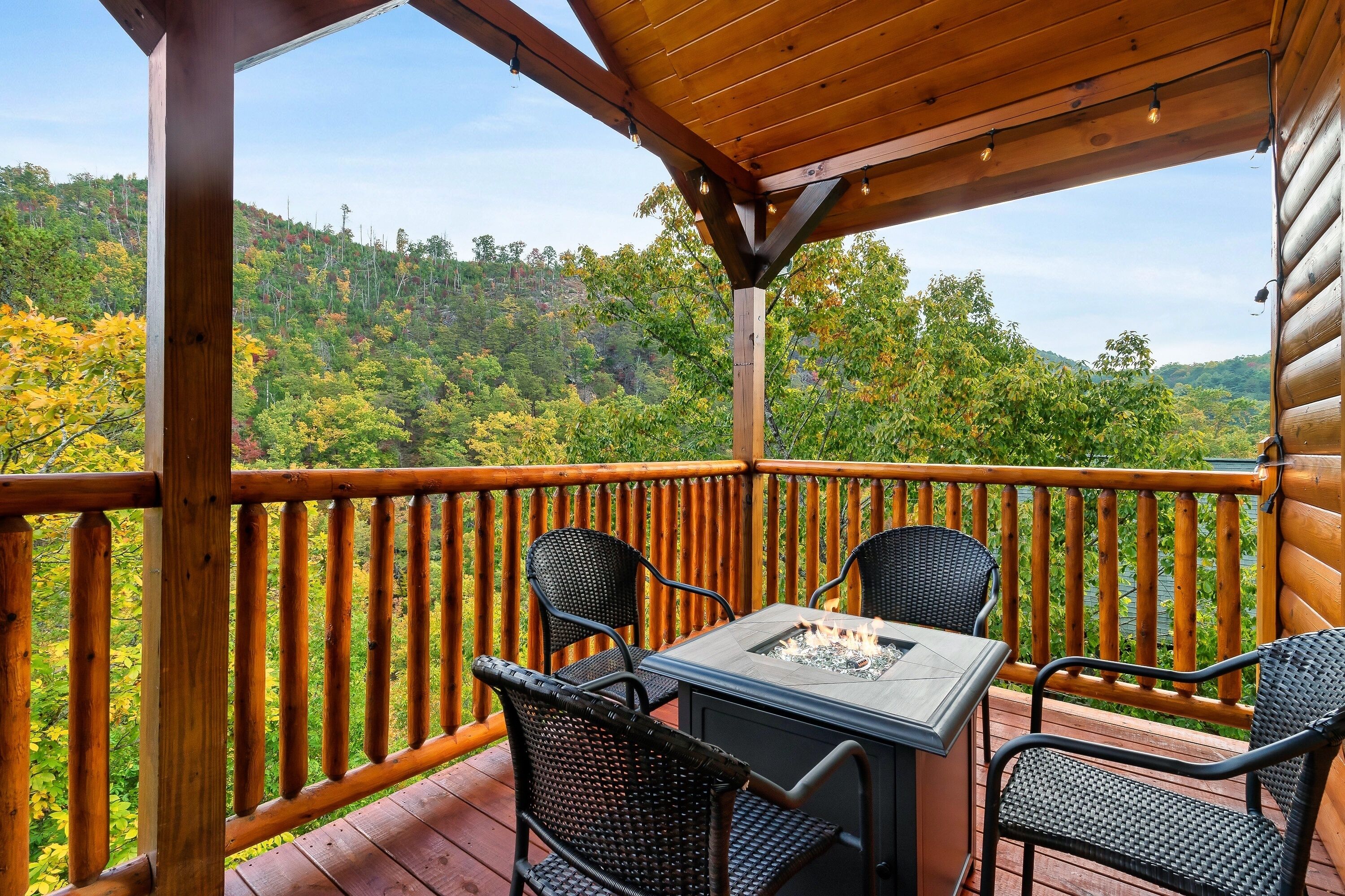 A wooden deck with a table and chairs, overlooking a forested hillside.