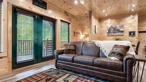 L’intérieur d’un chalet en bois, avec un canapé en cuir, un tapis à motifs et un tableau encadré au mur.