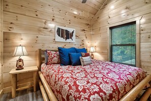 A wooden cabin bedroom with a bed, two nightstands, a map on the wall, and a window with blinds.