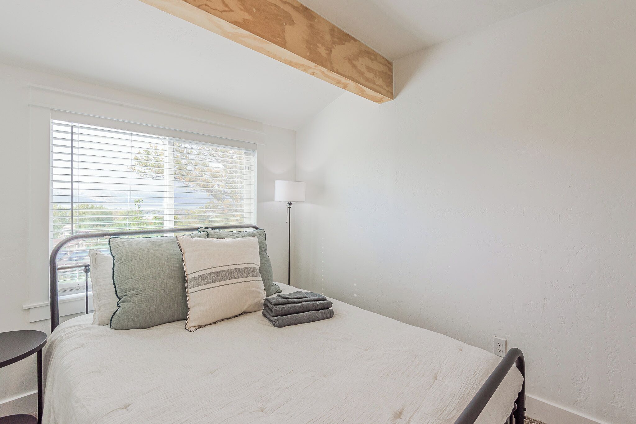 A bedroom with a bed, a bedside table, a lamp, and a window with blinds.