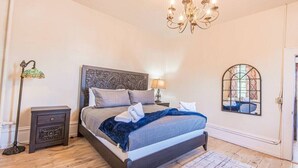 A bedroom with a bed, a nightstand, a lamp, a chandelier, and a window.