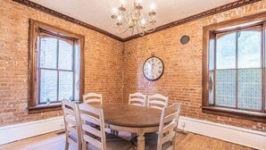 A dining room with a brick wall, a round table, six chairs, and a clock on the wall.