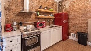 Una cucina compatta con parete in mattoni, mobili bianchi, un frigorifero rosso e un fornello.