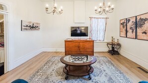 Un soggiorno con un mobiletto in legno, una televisione, un lampadario e un tappeto decorato.