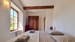 A room with two beds, a wooden wardrobe, and a window with a view of greenery.