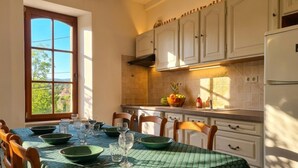 A dining area with a table set for four, a window with a view of greenery, and a kitchen with white cabinets and a refrigerator.
