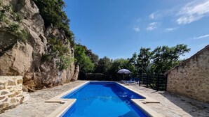 A rectangular swimming pool with a tiled edge, surrounded by stone walls and vegetation.