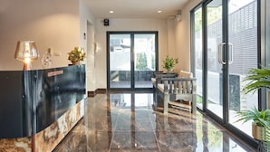 A reception area with a marble floor, a reception desk, a seating area with a bench, and large windows offering a view of the outside. - Be Phrasingh Hotel Chiang Mai (Chiang Mai)