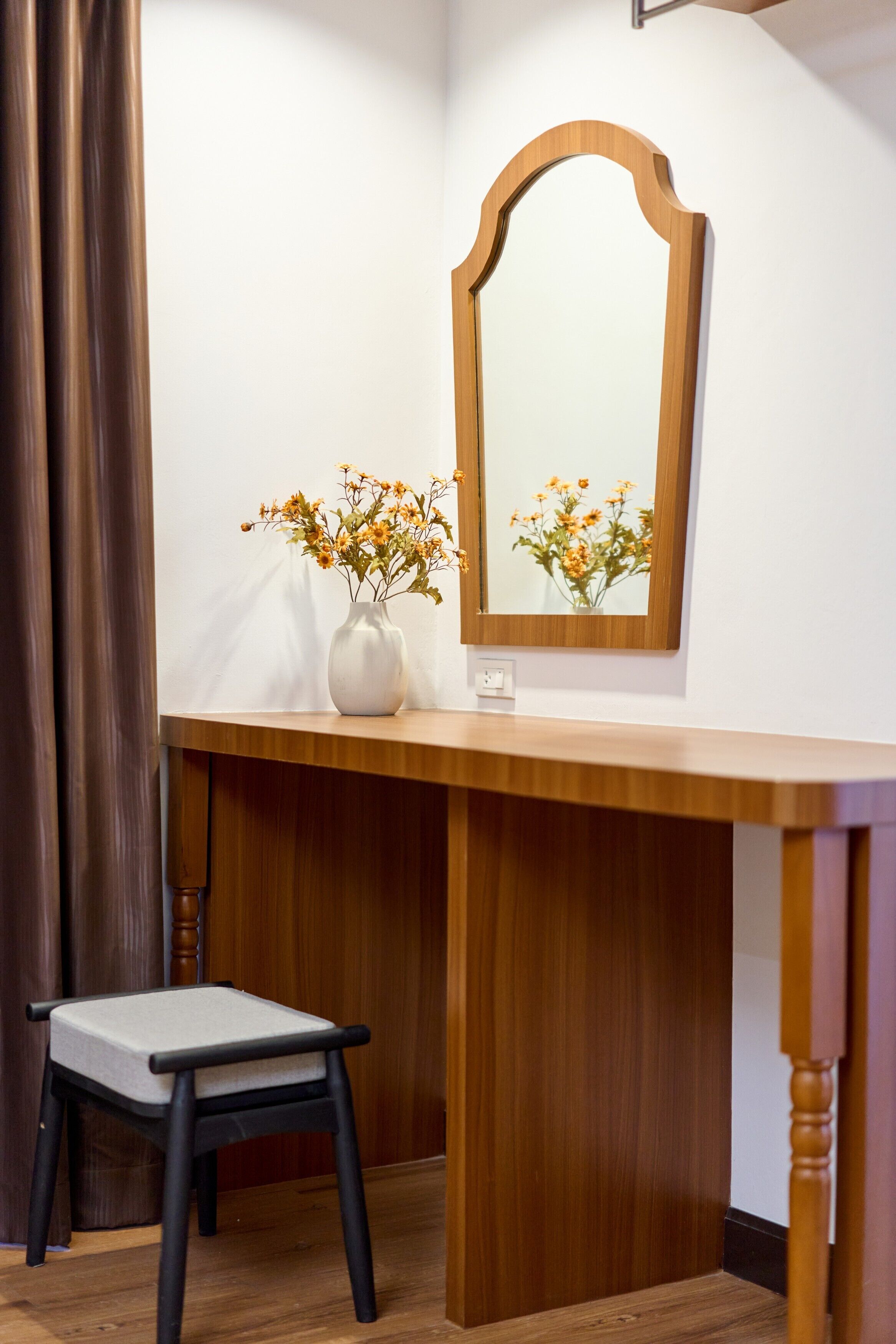 Un bureau en bois, un miroir, un vase avec des fleurs et une chaise.