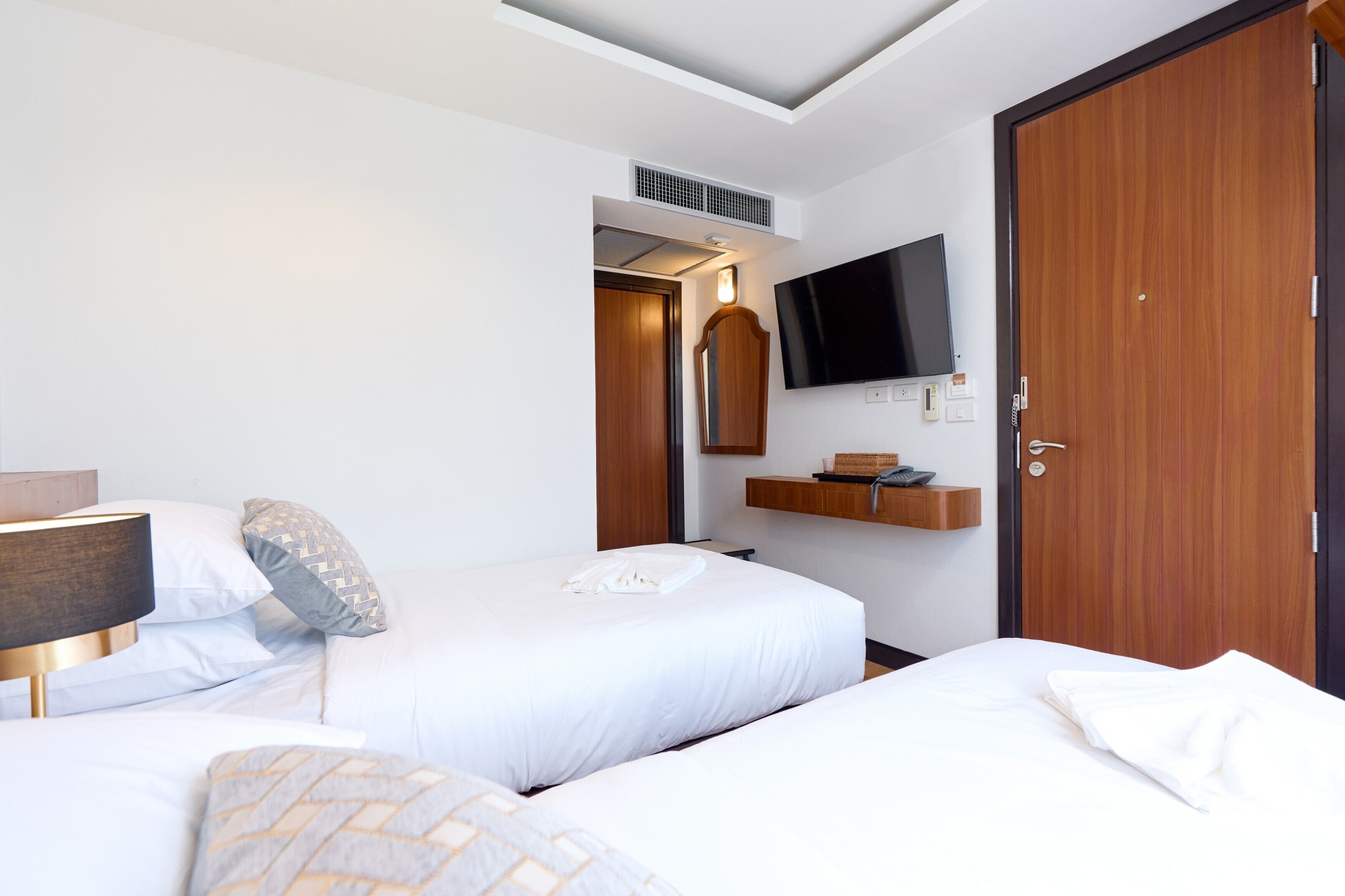 Een hotelkamer met twee bedden, een aan de muur bevestigde televisie, een houten garderobe en een plank met een telefoon en een mandje.