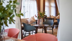 A modern dining area with a round table, blue chairs, and a vase with flowers. - Be Phrasingh Hotel Chiang Mai (Chiang Mai)