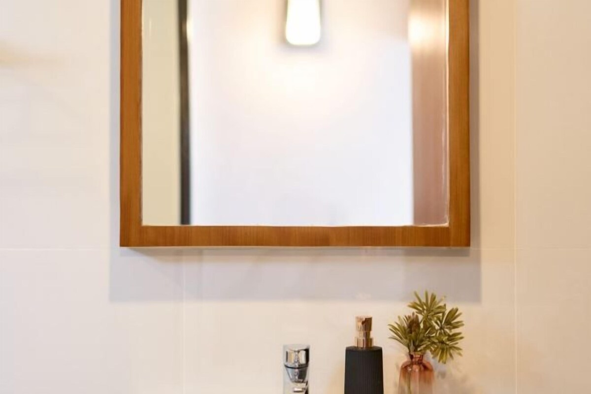 A bathroom with a wooden-framed mirror, a modern faucet, and a small plant on the counter.